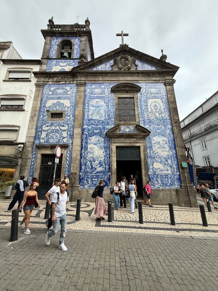 Facciata principale della Cappella delle Anime di Porto decorata con tipici azulejos blu e bianchi, raffiguranti scene religiose, con turisti davanti all’ingresso.