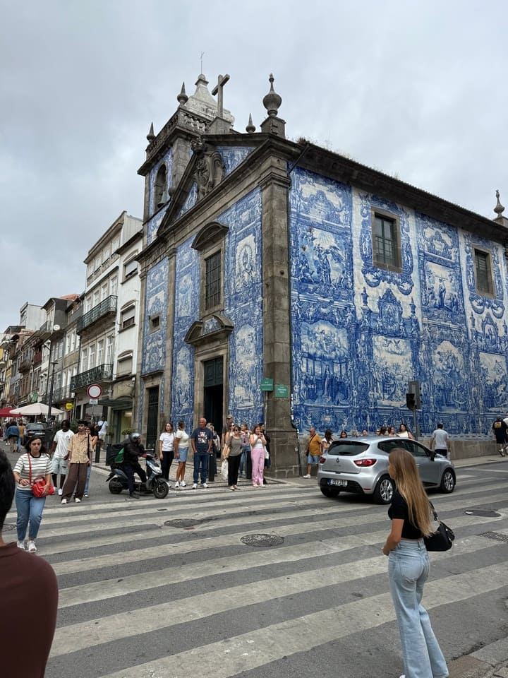 Vista laterale della Cappella delle Anime a Porto, interamente ricoperta di azulejos blu e bianchi, lungo una strada trafficata con pedoni e veicoli.