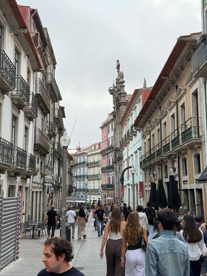 Passeggiata animata lungo Rua das Flores a Porto, via pedonale storica con edifici eleganti e caffè.