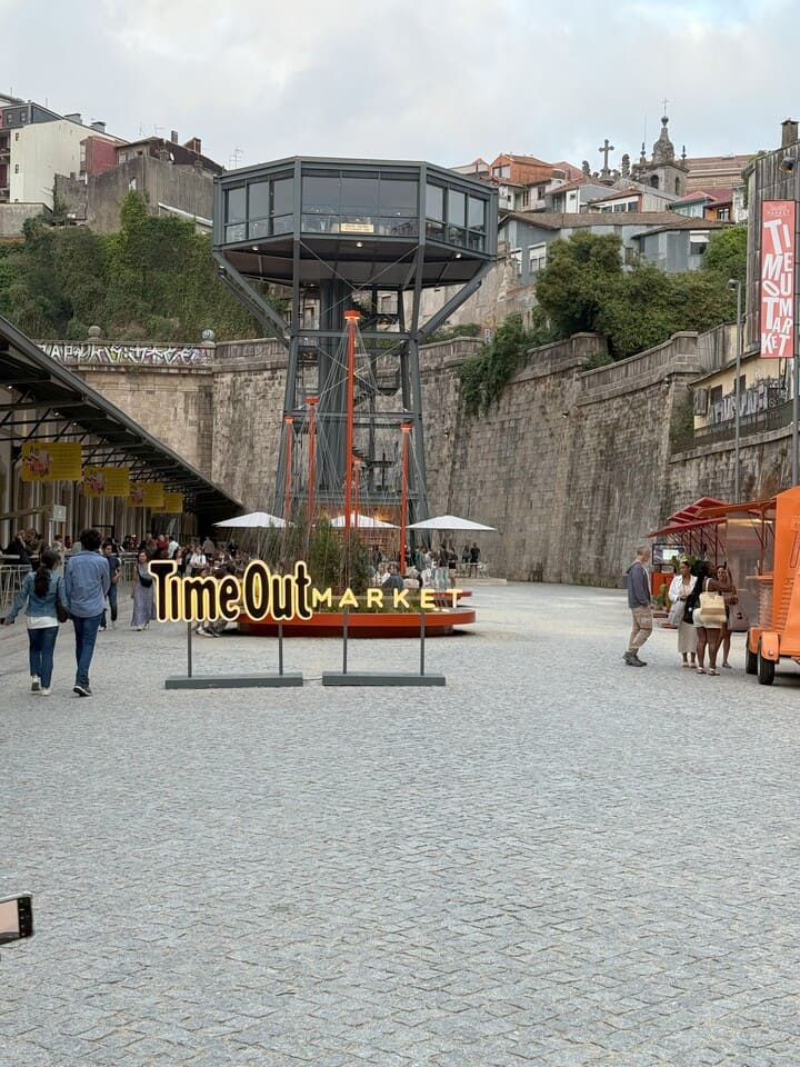 Vista esterna del Time Out Market di Porto con insegna luminosa e struttura panoramica sopraelevata, in un’area pedonale frequentata da visitatori.