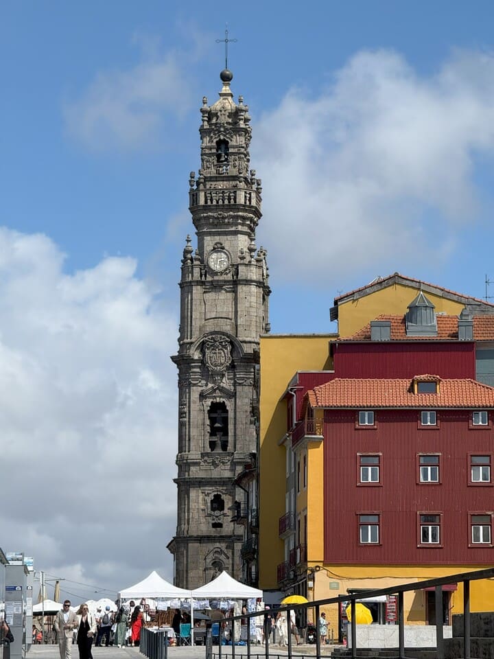 Veduta della Torre dos Clérigos di Porto, simbolo barocco della città, con mercatino e case colorate in primo piano.