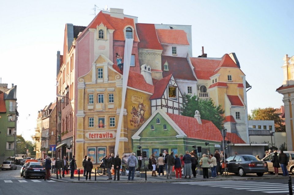 Murale di Śródka a Poznań, colorata opera d’arte urbana che racconta la storia del quartiere con case e personaggi in 3D.