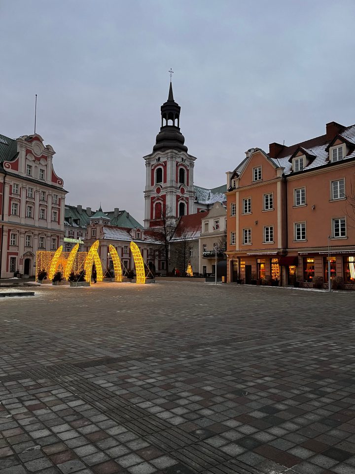 Plac Kolegiacki a Poznań al tramonto con le decorazioni luminose e la Chiesa di San Stanislao sullo sfondo.
