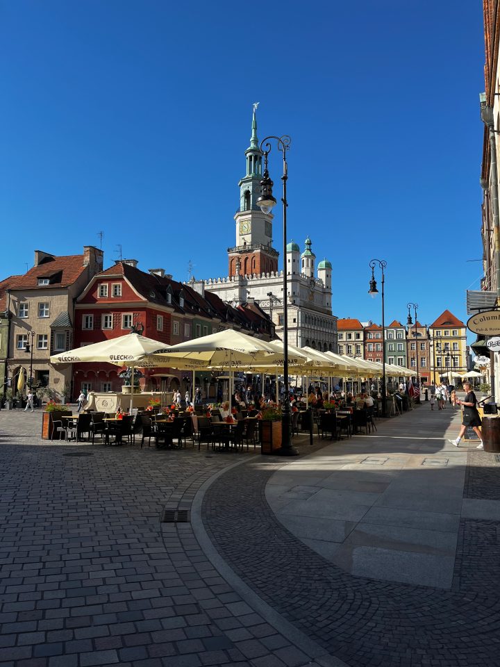 Piazza Stary Rynek a Poznań con il Municipio rinascimentale sullo sfondo e caffè all’aperto sotto grandi ombrelloni.