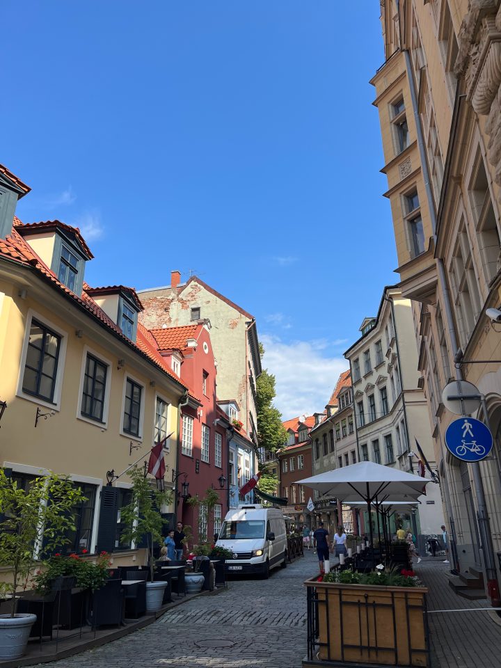 Stradina acciottolata della città vecchia di Riga con case colorate, caffè all’aperto e atmosfera tipica del centro storico lettone.