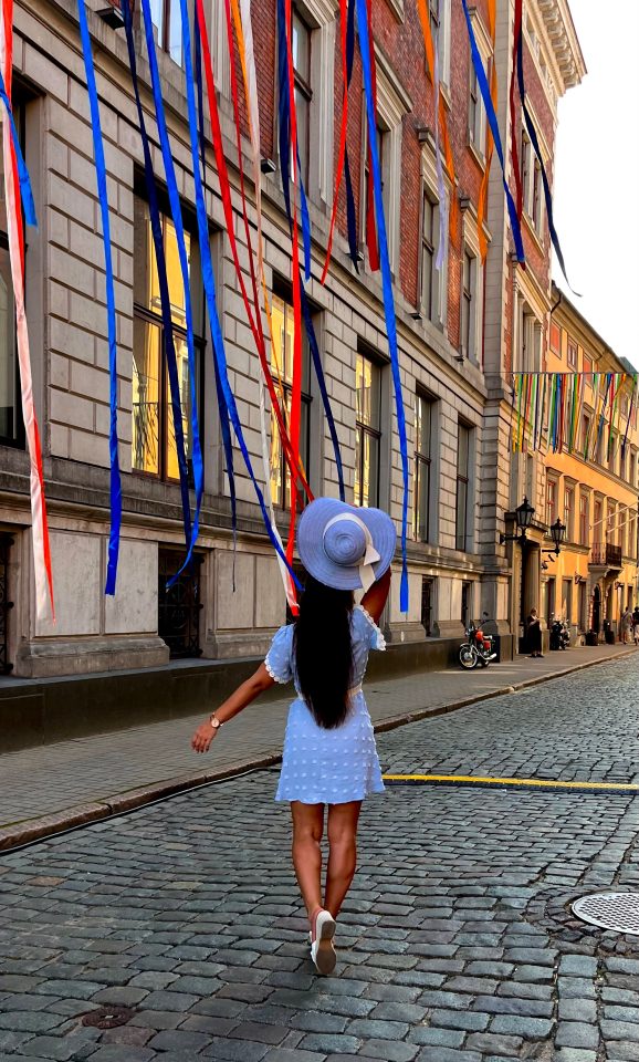 Ragazza con cappello passeggia tra i nastri colorati nelle strade della città vecchia di Riga durante un festival estivo.