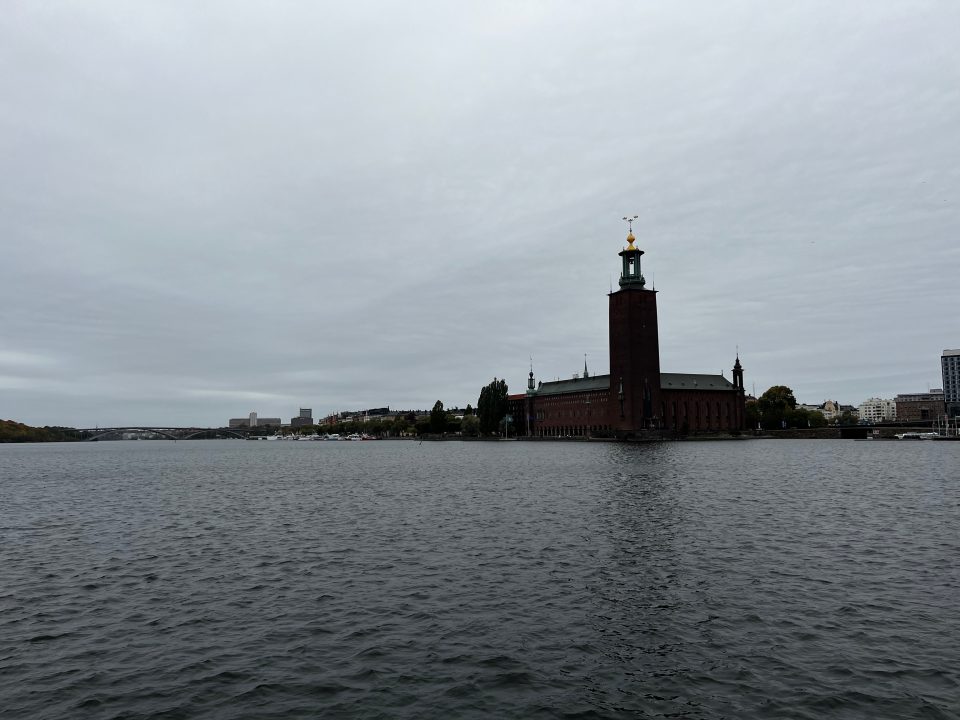 Vista panoramica del Municipio di Stoccolma (Stadshuset) con la torre delle tre corone dorate riflessa sull’acqua.