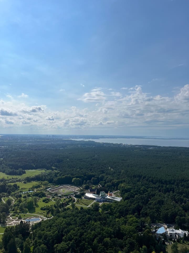 Panorama che mostra un paesaggio verdeggiante con una vista sul Mar Baltico e un cielo azzurro con nuvole sparse.